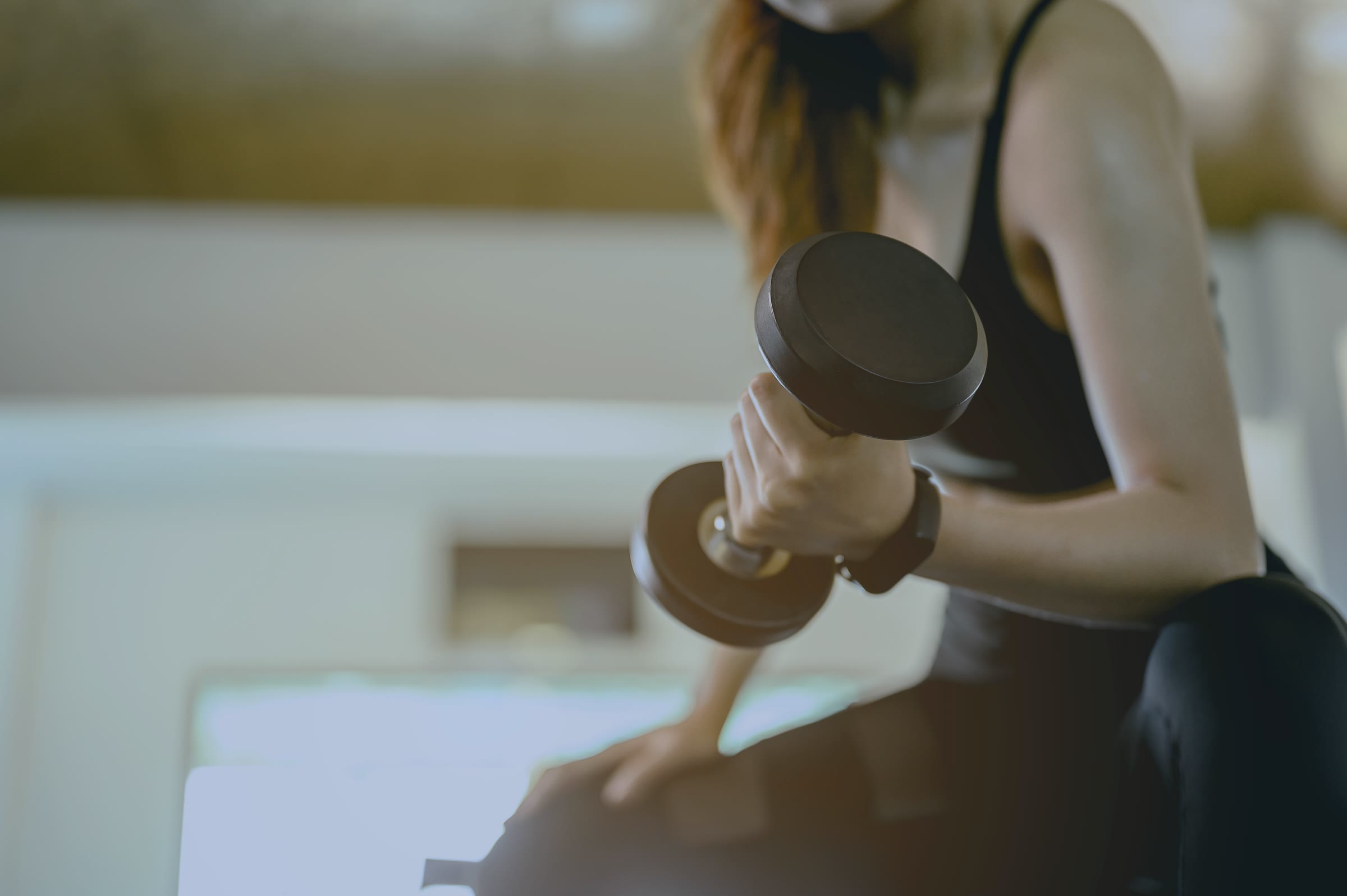 A woman curling a dumbbell, seated in a gym